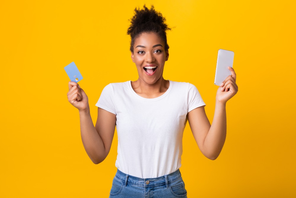excited-black-lady-holding-credit-card-and-cellpho-2023-11-27-05-27-25-utc